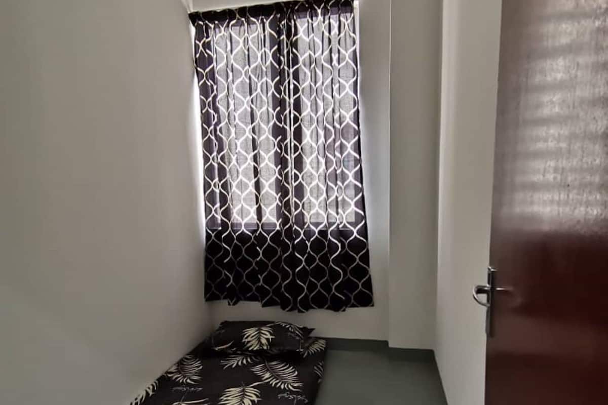 A small room with a single bed, a window with patterned curtains, and a door.