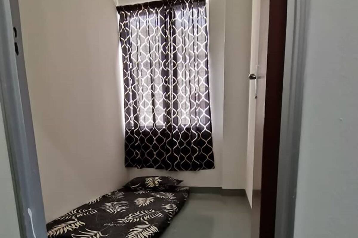 A narrow hallway with a bed at the end, a window with patterned curtains, and a door on the right.