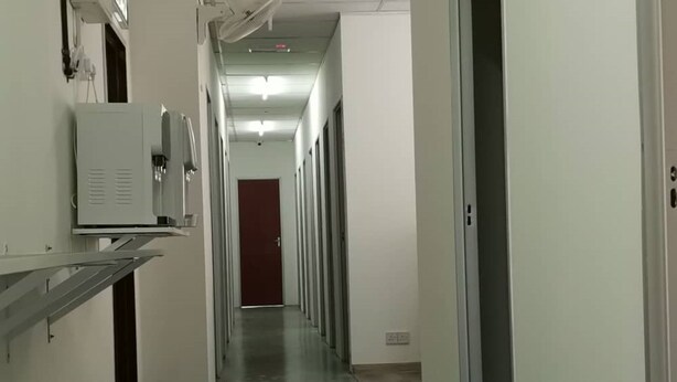 A long, narrow hallway with a red door at the end, white walls, and a metal handrail on the left. - Spot ON 90500 Sri Rampai Metro Hostel (Kuala Lumpur)