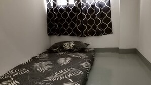 A small, single-bed room with a patterned bedspread, a window with a decorative screen, and a plain white wall. - Spot ON 90500 Sri Rampai Metro Hostel (Kuala Lumpur)