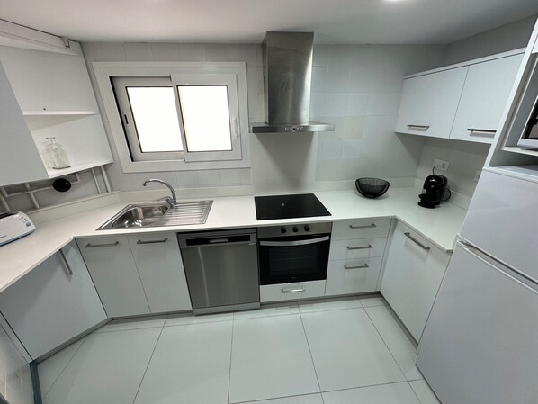 A modern kitchen with white cabinets, a stainless steel sink, a dishwasher, an oven, and a black coffee maker.