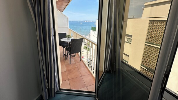 Un balcone con vista sul mare, un tavolo e delle sedie.