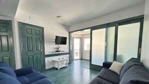 Un soggiorno con divano, televisione a parete, un tavolino e una porta scorrevole in vetro che dà su un balcone.