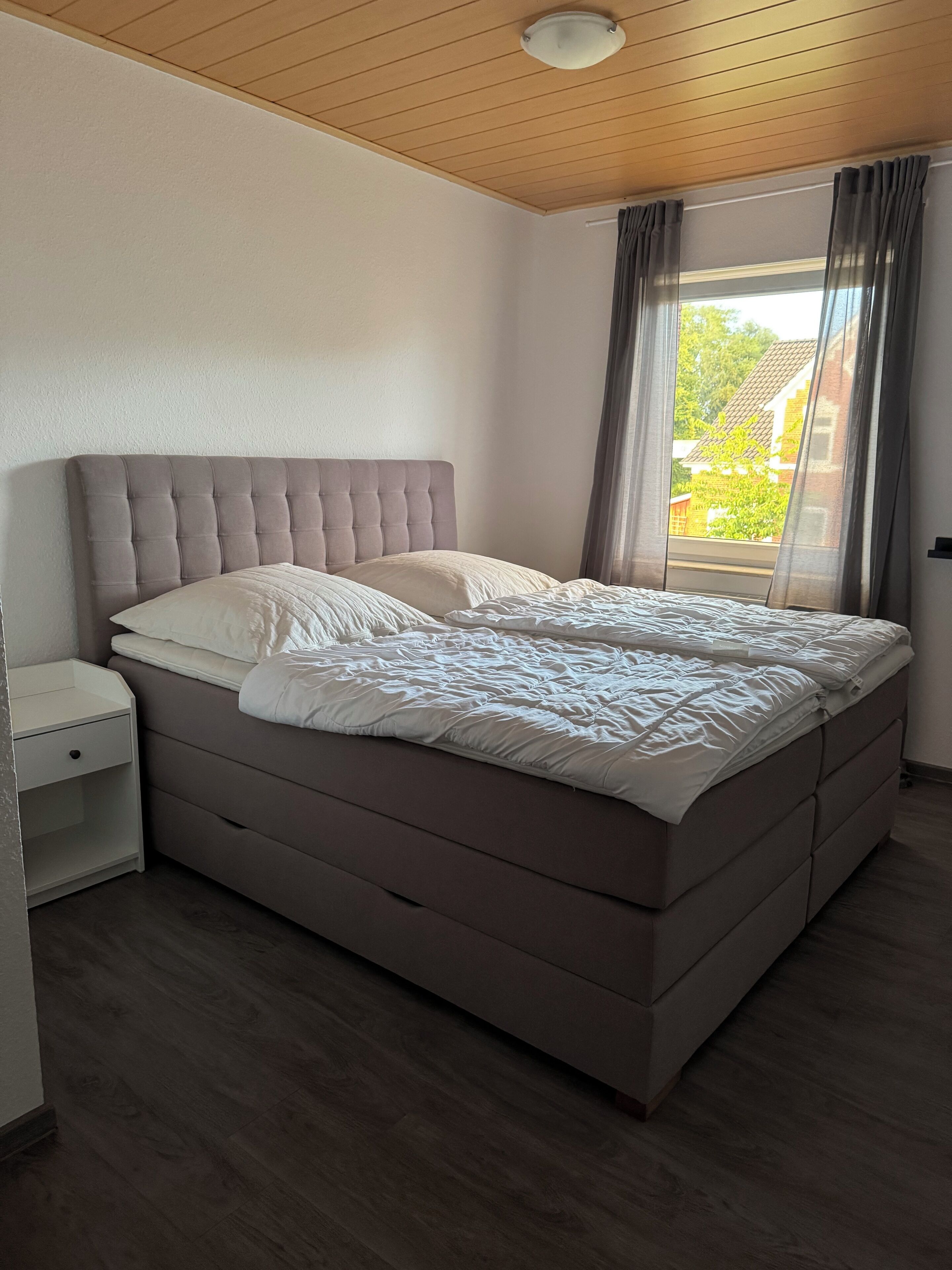 Een slaapkamer met een groot bed, een nachtkastje en een raam met gordijnen.