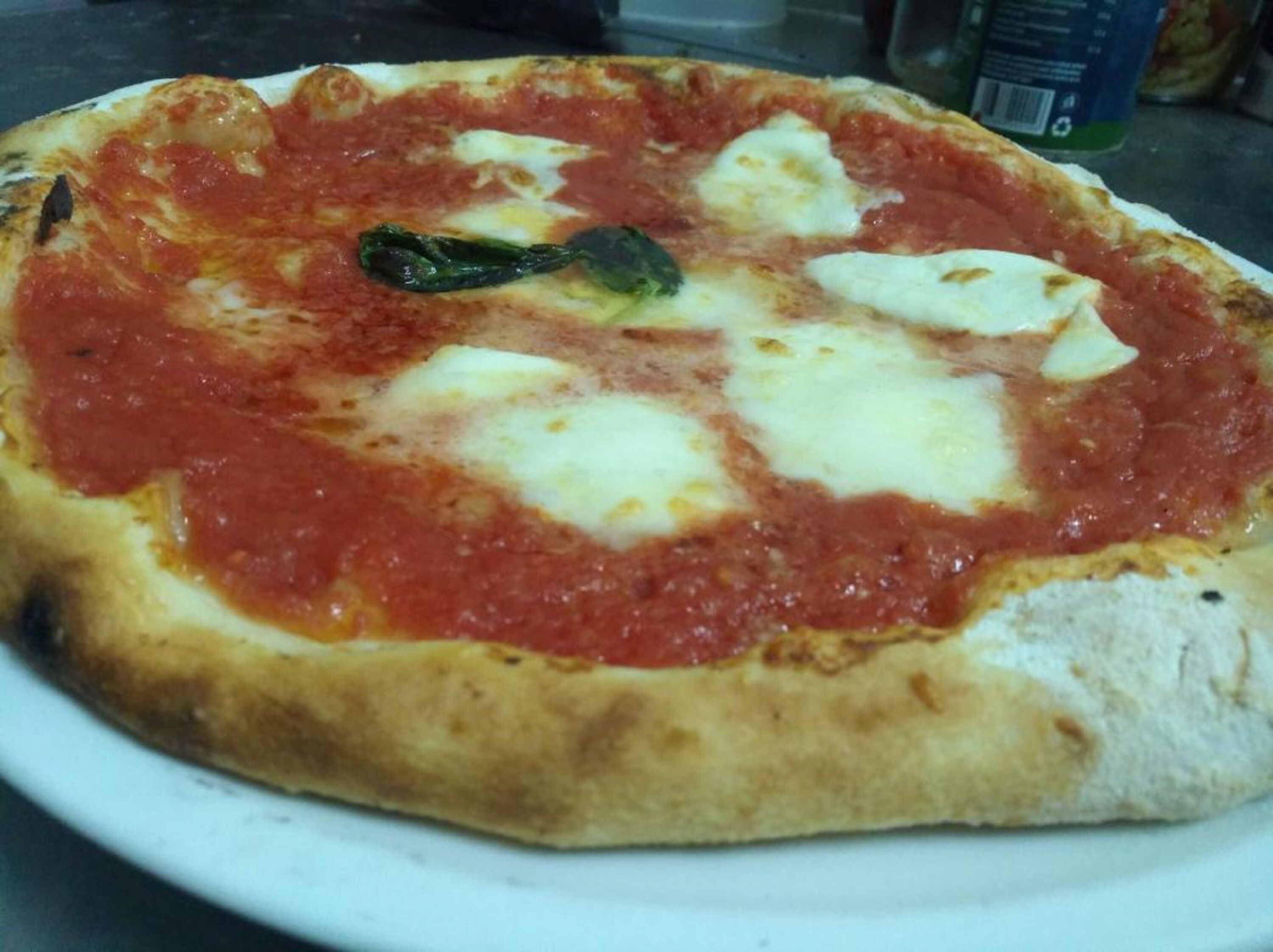 A pizza with tomato sauce, cheese, and a basil leaf on a white plate.
