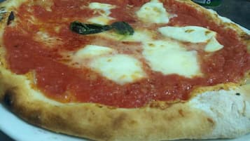 A pizza with tomato sauce, cheese, and a basil leaf on a white plate.