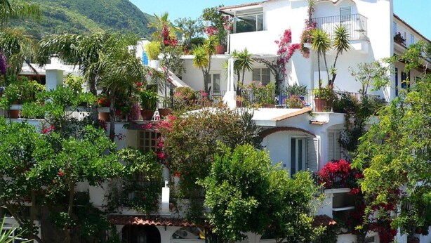 A white building with balconies, surrounded by lush greenery and flowering plants. - Hotel La Maggioressa (Casamicciola Terme)