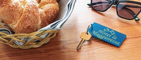 A wicker basket with bread, a pair of sunglasses, and a hotel keychain on a wooden surface.