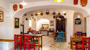 A dining area with wooden tables and chairs, a tiled floor, and hanging baskets. - Hotel La Maggioressa (Casamicciola Terme)