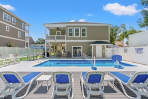 Ein zweistöckiges Gebäude mit Swimmingpool und Liegestühlen.