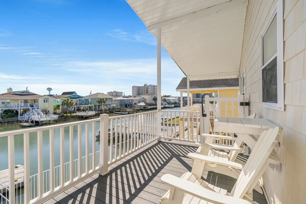 A wooden deck with white railings overlooking a marina with boats and buildings in the background.