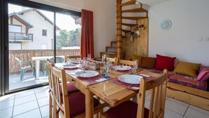 A dining area with a wooden table set for four, a wooden staircase, and a sofa with cushions. - Le Bleuet du Lac - Appartement avec Terrasse Vue Lac (Savines-le-Lac)