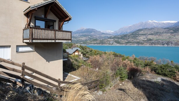 A mountain cabin with a balcony overlooking a lake and mountains. - Le Bleuet du Lac - Appartement avec Terrasse Vue Lac (Savines-le-Lac)