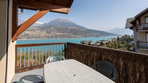 A balcony with a table and chairs, overlooking a lake and mountains. - Le Bleuet du Lac - Appartement avec Terrasse Vue Lac (Savines-le-Lac)