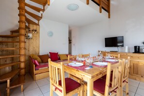 A wooden dining area with a spiral staircase, a sofa with cushions, and a television on the wall.