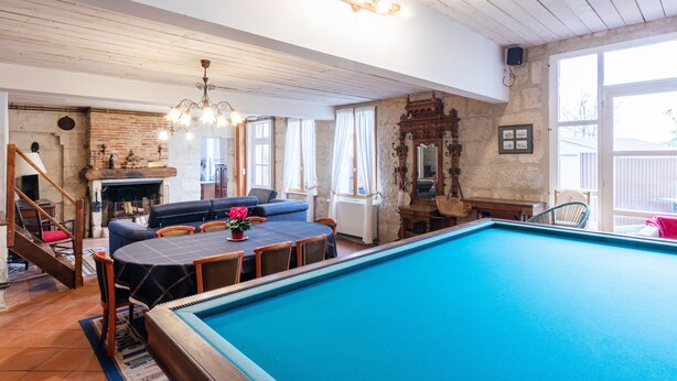 Un espace piscine aménagé avec une table et des chaises, un canapé et un escalier menant à une mezzanine.