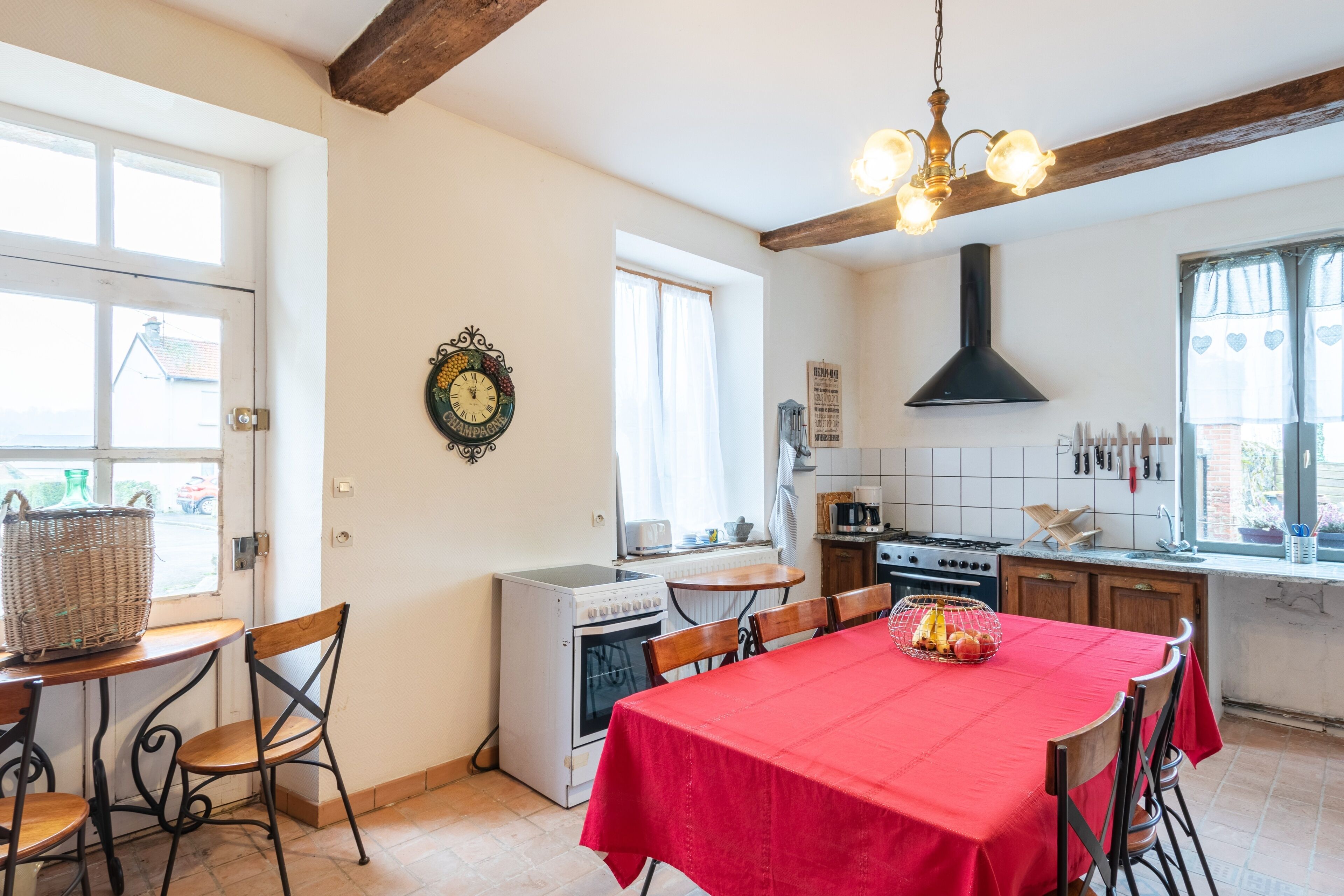 Une cuisine avec une table rouge, des chaises en bois, un four blanc et une hotte noire.