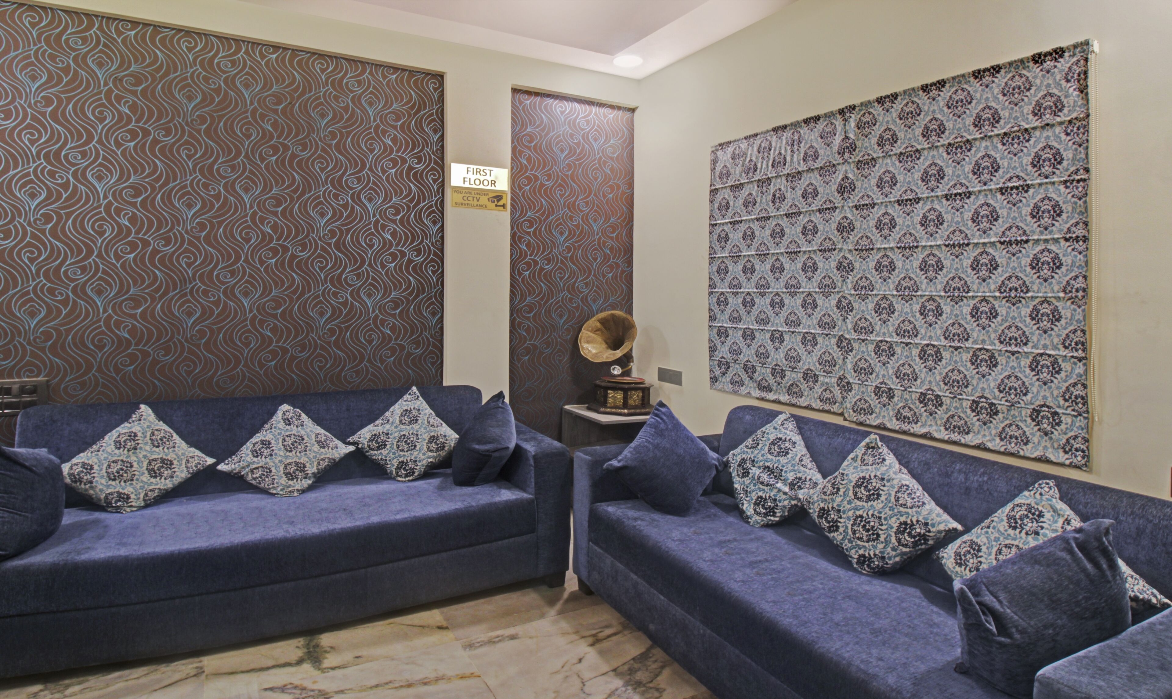 A room with two blue sofas, patterned cushions, a wall with a decorative pattern, and a sign indicating the first floor.