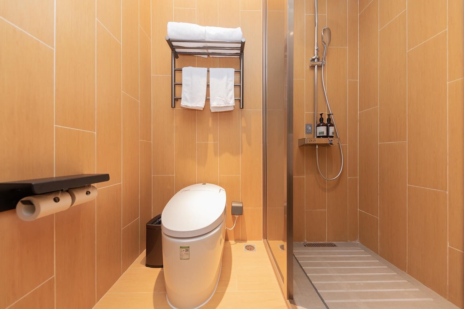 Une salle de bain équipée de toilettes, d’un porte-serviettes, d’une douche et d’une poubelle.
