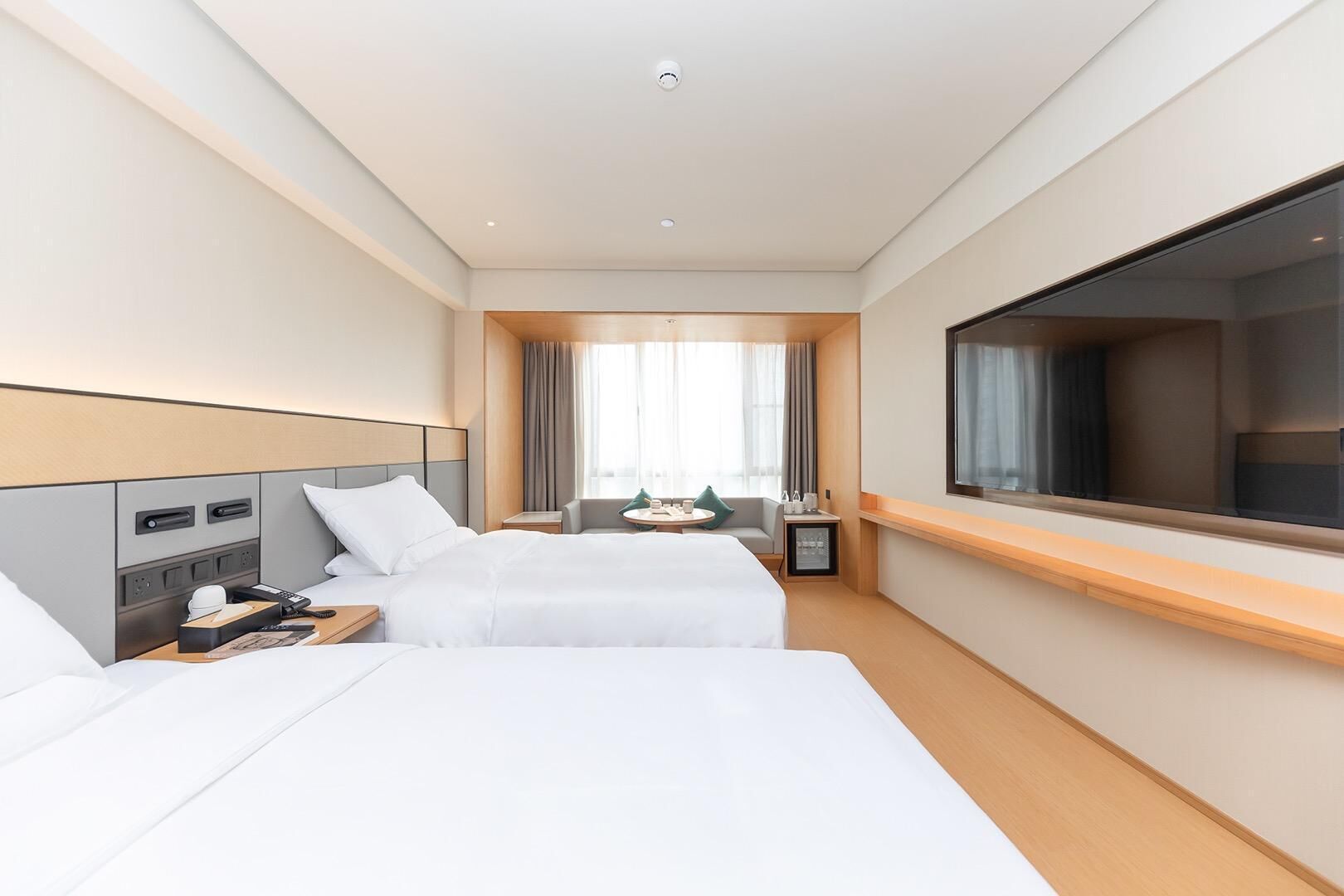 A hotel room with two beds, a TV, a desk with a chair, and a window with curtains.