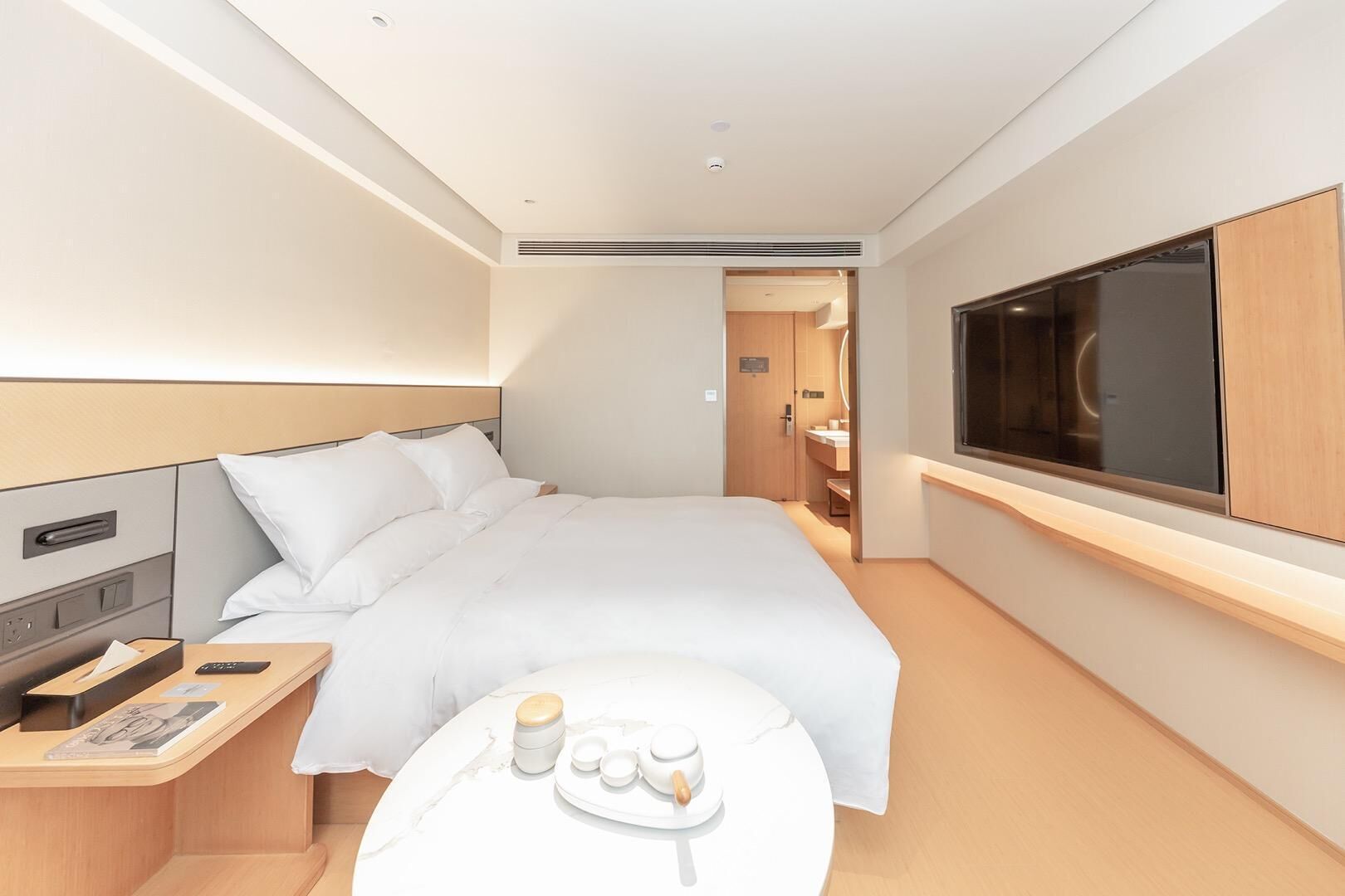 Une chambre d’hôtel moderne avec un grand lit, une table de chevet, une télévision et une petite table avec des articles de toilette.