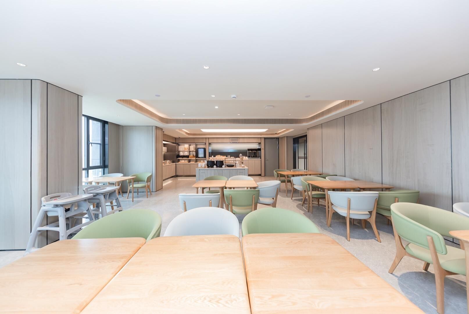 A spacious dining area with multiple tables and chairs, a kitchen in the background, and a modern interior design.