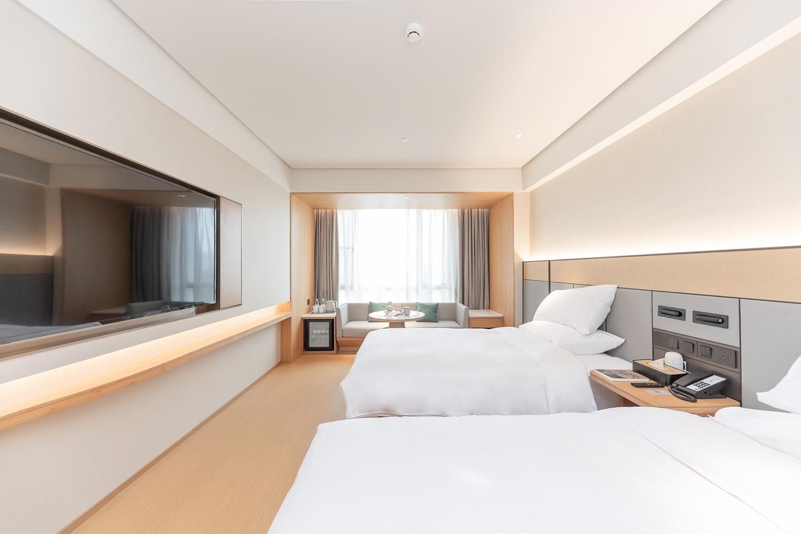 A hotel room with two beds, a TV, a desk, a chair, and a window with curtains.