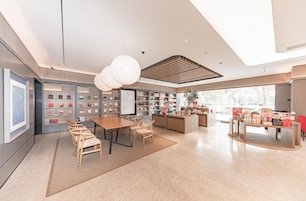 Un interior moderno con una zona de comedor central, estantes con objetos y un amplio ventanal.