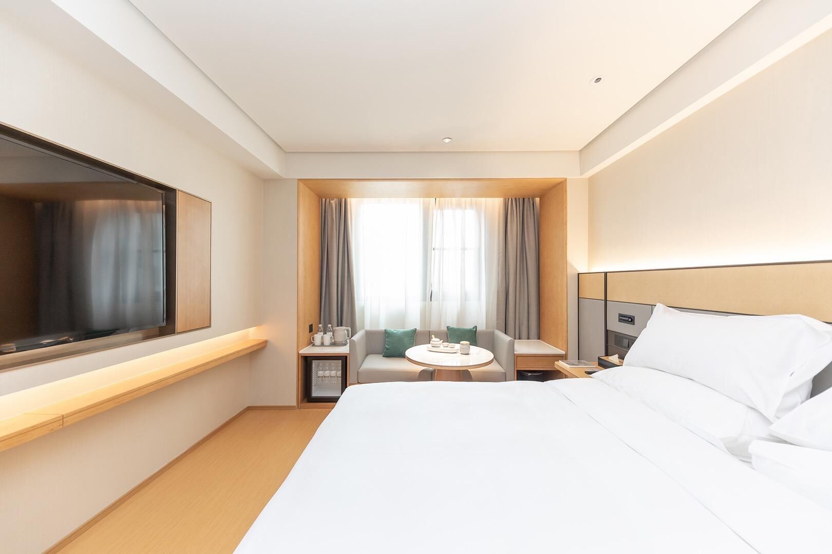 A hotel room with a bed, a TV, a small table with a chair, and a window with curtains.