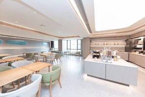 A modern dining area with tables and chairs, a kitchen counter with appliances, and large windows.