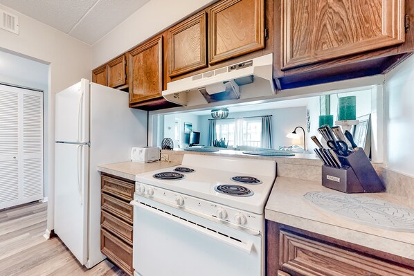Kitchen features a central stove, oven, microwave, and sink with a knife block, offering a view of the adjacent living area.