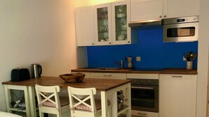 A compact kitchen with white cabinets, a blue backsplash, and a wooden dining table with two chairs.