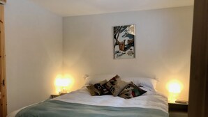 A neatly made bed with a green blanket, two bedside lamps, and a framed picture on the wall.