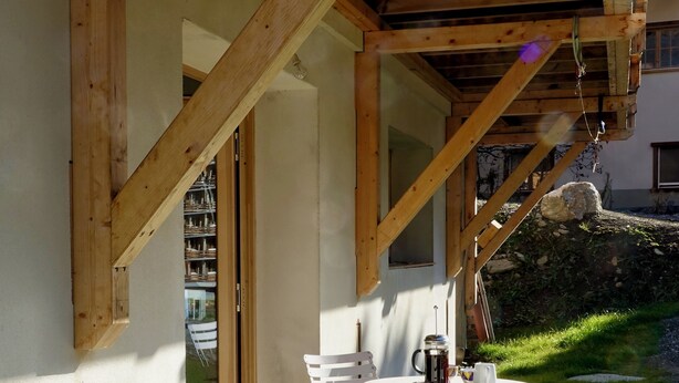 A wooden deck with a table and chairs, a potted plant, and a stone wall.