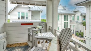 Eine überdachte Veranda mit Adirondack-Stühlen und einem kleinen Tisch, mit Blick auf eine Reihung weißer Häuser mit grünen Fensterläden.