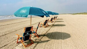 Ein Strand mit Reihen von Liegestühlen und Sonnenschirmen, jeweils beschriftet mit 'Palmilla Beach Resort & Golf Community'.