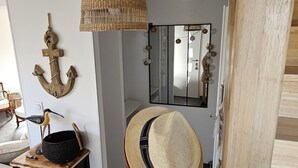 Una habitación con una silla de madera, una lámpara colgante tejida, un espejo en la pared y un aparador con cajones.