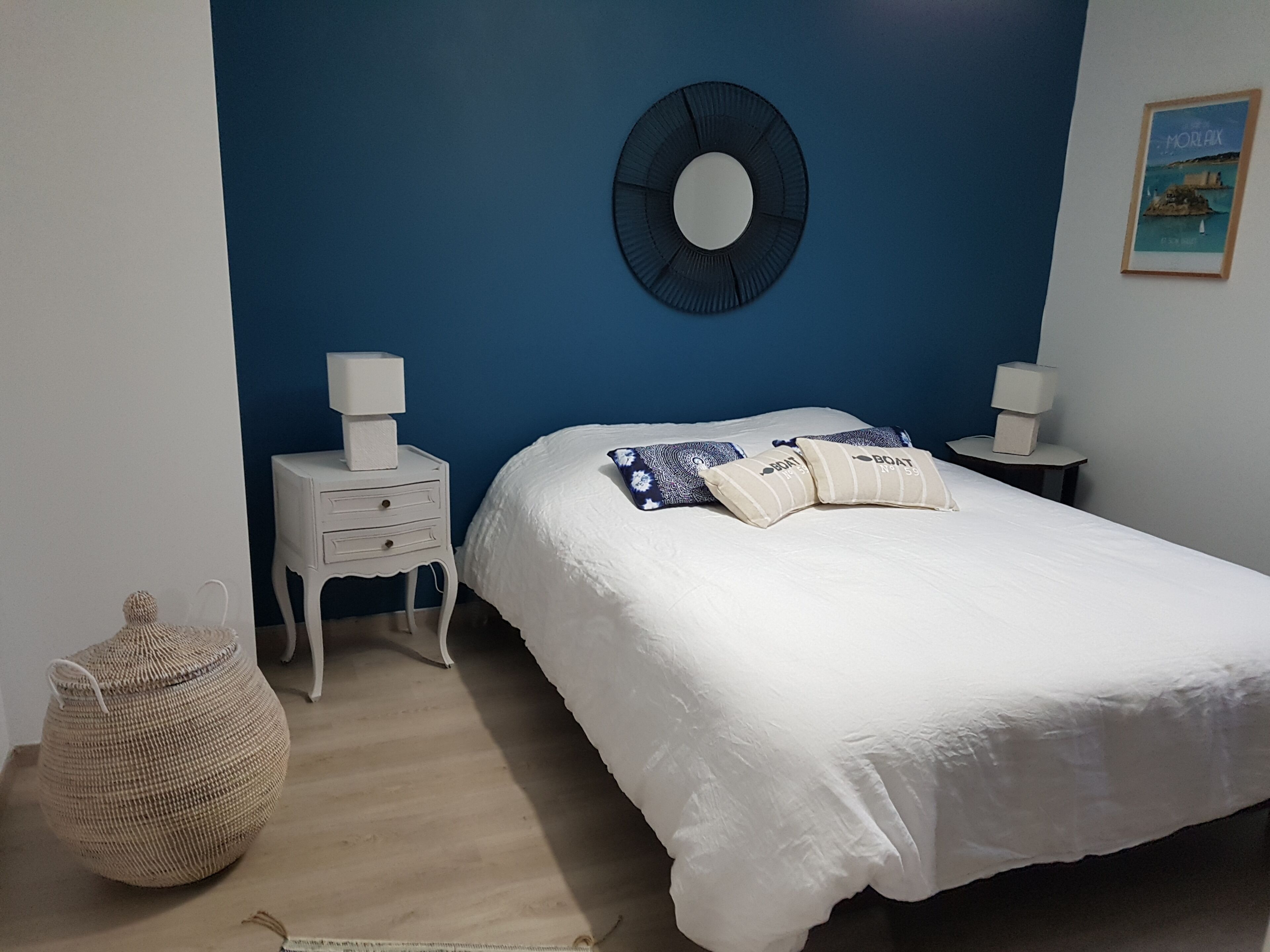 Un dormitorio con una cama, dos mesitas de noche, un reloj de pared, una cesta tejida y un cuadro enmarcado.