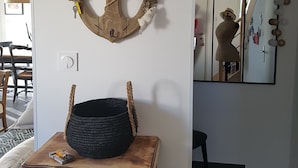 Una habitación con una decoración de ancla de madera, una cesta tejida negra sobre una mesa de madera, un espejo y un colgador de luz.