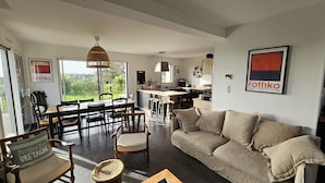 Una sala de estar moderna con sofá, sillas, una mesa de comedor y una cocina al fondo.