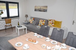A modern living room with a grey sofa, colorful pillows, a dining table set with plates, cups, and a teapot. - New flats In the historic old town in the pedestrian zone (Dillenburg)