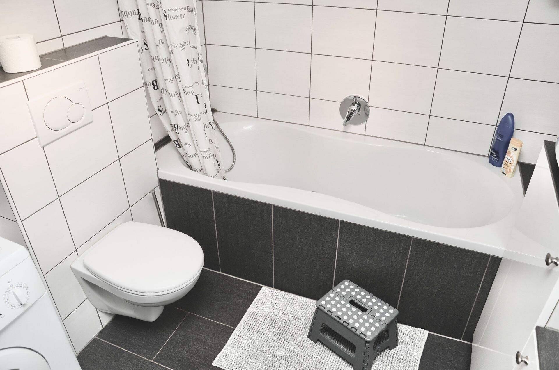 Un baño con inodoro, bañera, cortina de ducha y un taburete.