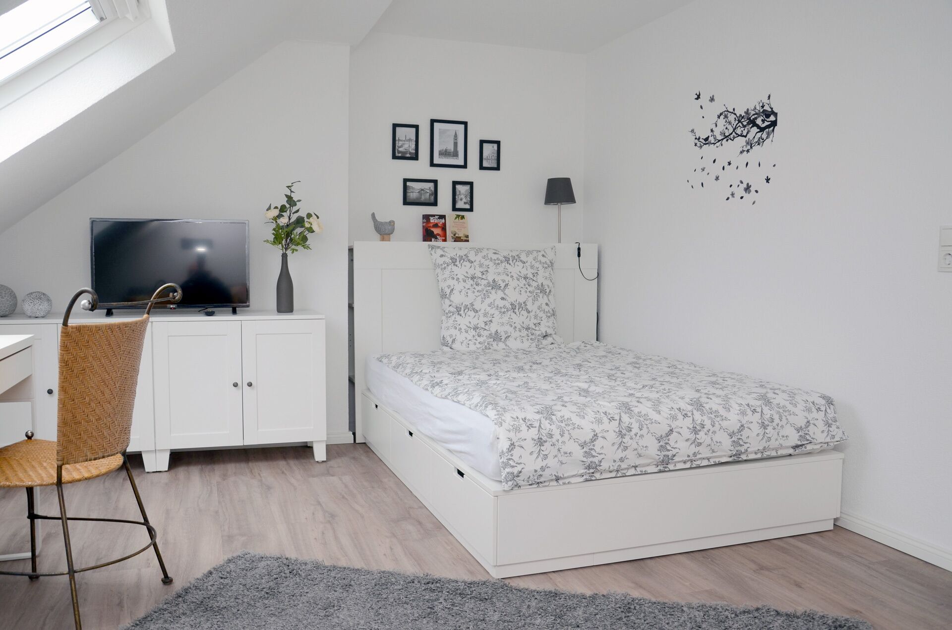 A bedroom with a bed, a desk with a TV, a chair, and a small plant.