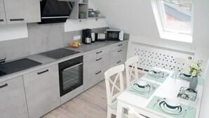 A modern kitchen with grey cabinets, a built-in oven, a microwave, and a dining area with a white table set for two. - New flats In the historic old town in the pedestrian zone (Dillenburg)