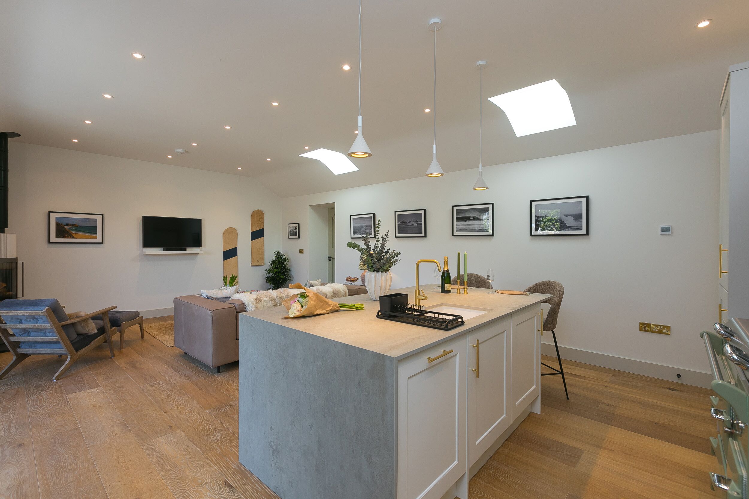 A modern kitchen with a central island, pendant lighting, and a flat-screen TV mounted on the wall.