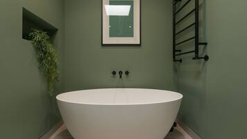Une salle de bain moderne avec une baignoire îlot, une œuvre d’art encadrée au-dessus de la baignoire et une petite plante dans un renfoncement.