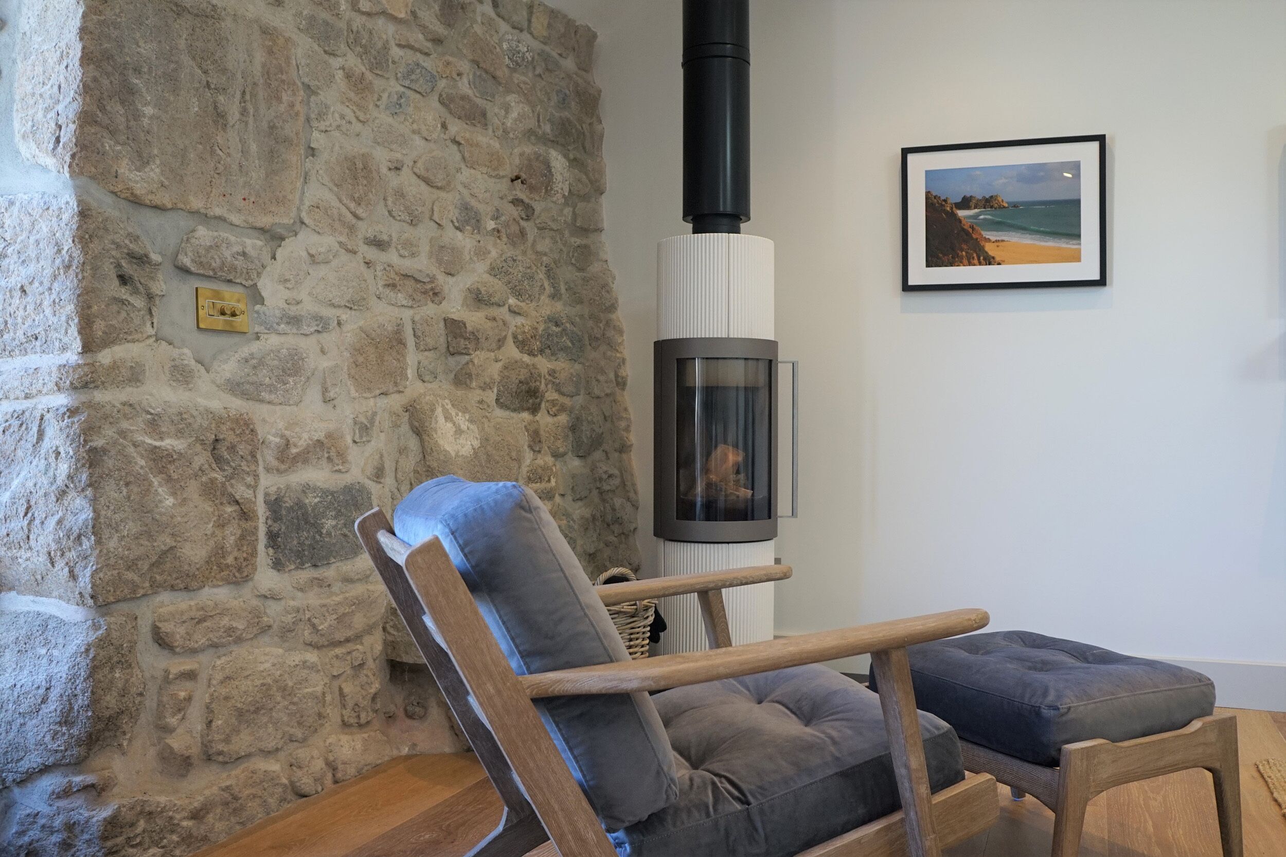 A stone wall, a wooden chair with a cushion, a framed picture, and a fireplace.