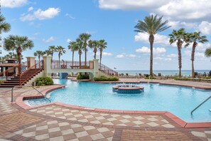 Relax by the ocean with a refreshing dip in the pool surrounded by palm trees and lounge chairs.