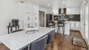 Una cocina moderna con gabinetes blancos, una isla de mármol y un salpicadero con diseño en espiga.