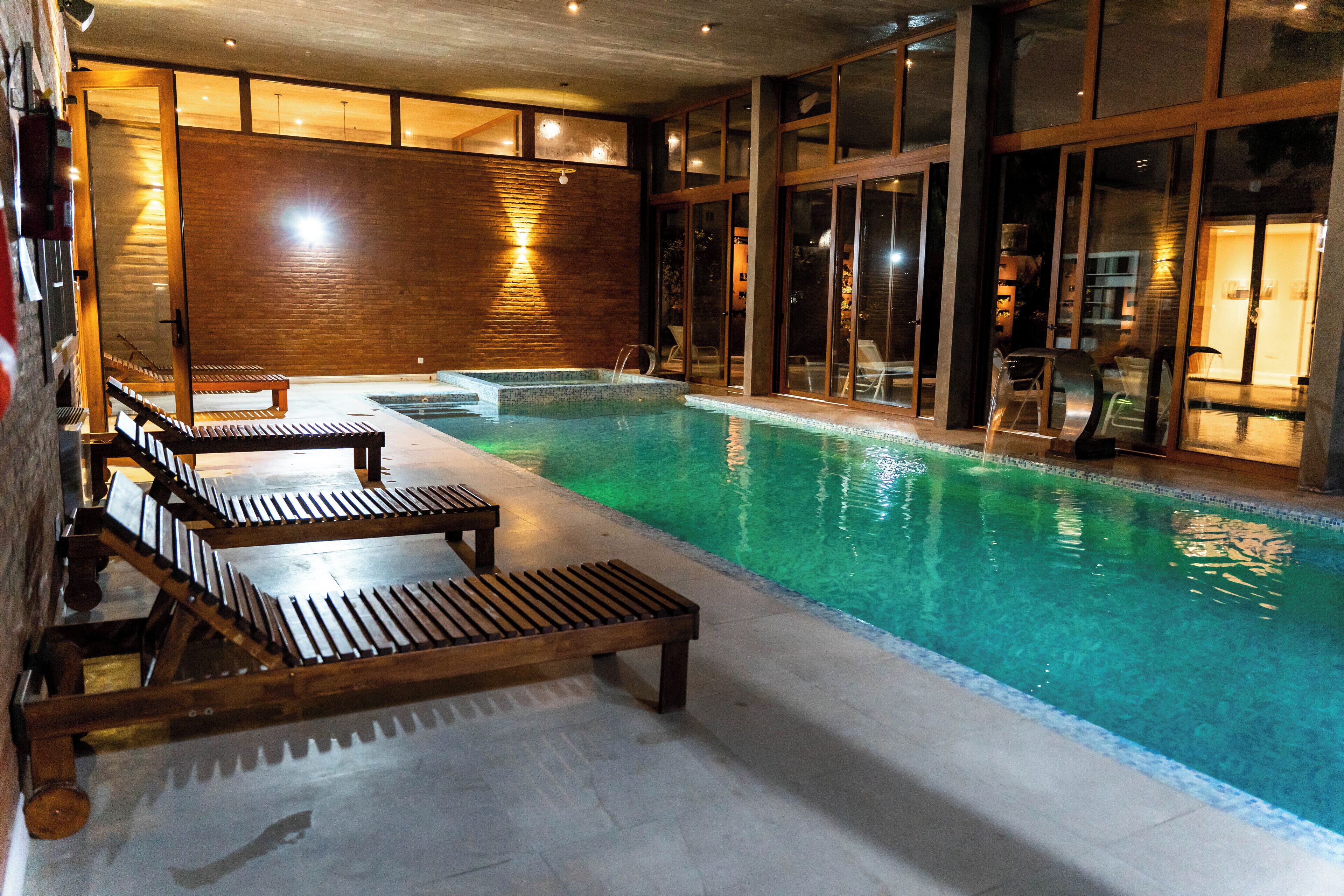 An indoor swimming pool with wooden loungers and a tiled floor.